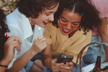Girl friends sat in park looking at a phone laughing