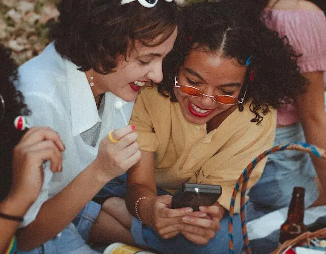 Girl friends sat in park looking at a phone laughing