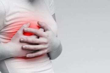 Breast pain. Woman suffering from painful feelings, clutching her boob, monochrome photo with red spot, panorama
